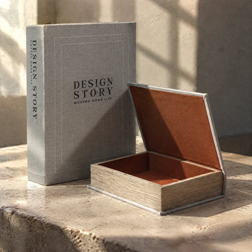 Γκρι κουτιά βιβλία Design Story σε πέτρινη επιφάνεια με ηλιακό φως, με το μικρό κουτί ανοιχτό