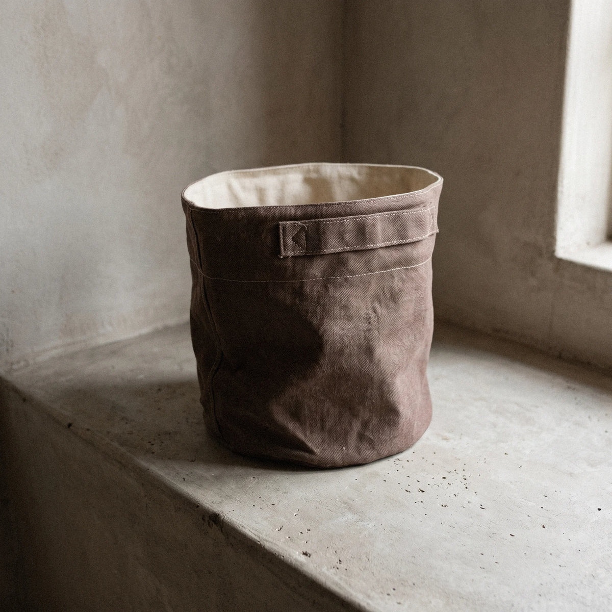 Υφασμάτινο καλάθι από καραβόπανο σε καφέ πούρου απόχρωση σε καλλιτεχνική διακοσμητική σύνθεση τύπου still life.